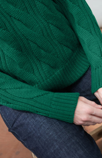 Close-up of a person wearing a green cable knit paul james sweater and dark jeans.