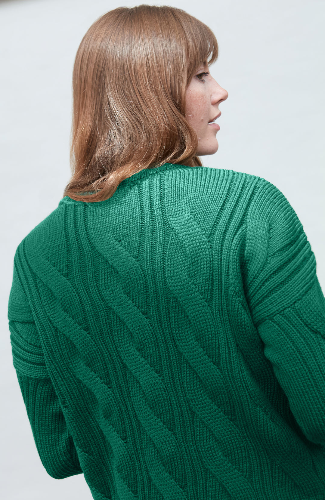 Woman wearing a green paul james wool cable knit sweater against a white background
