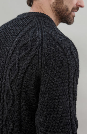 Man wearing a black wool cable sweater Made in England by Paul James Knitwear