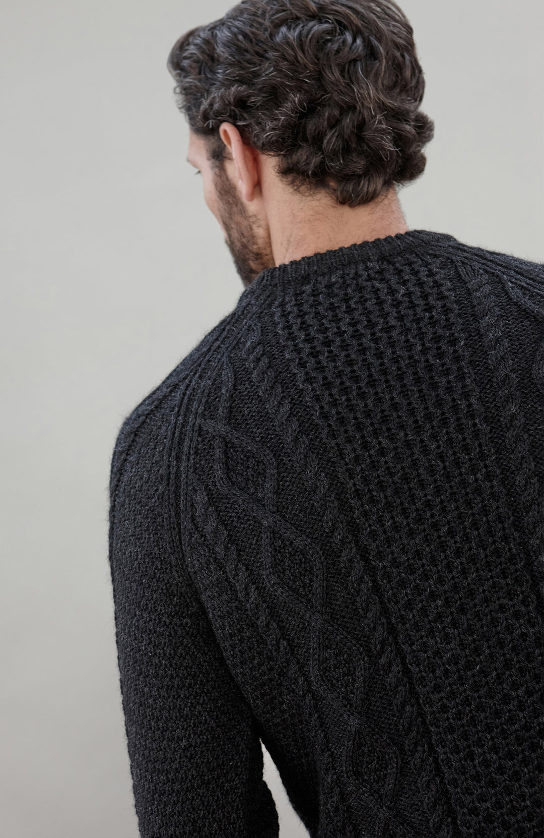 Man wearing a black wool cable sweater Made in England by Paul James Knitwear