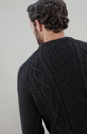 Man wearing a black wool cable sweater Made in England by Paul James Knitwear