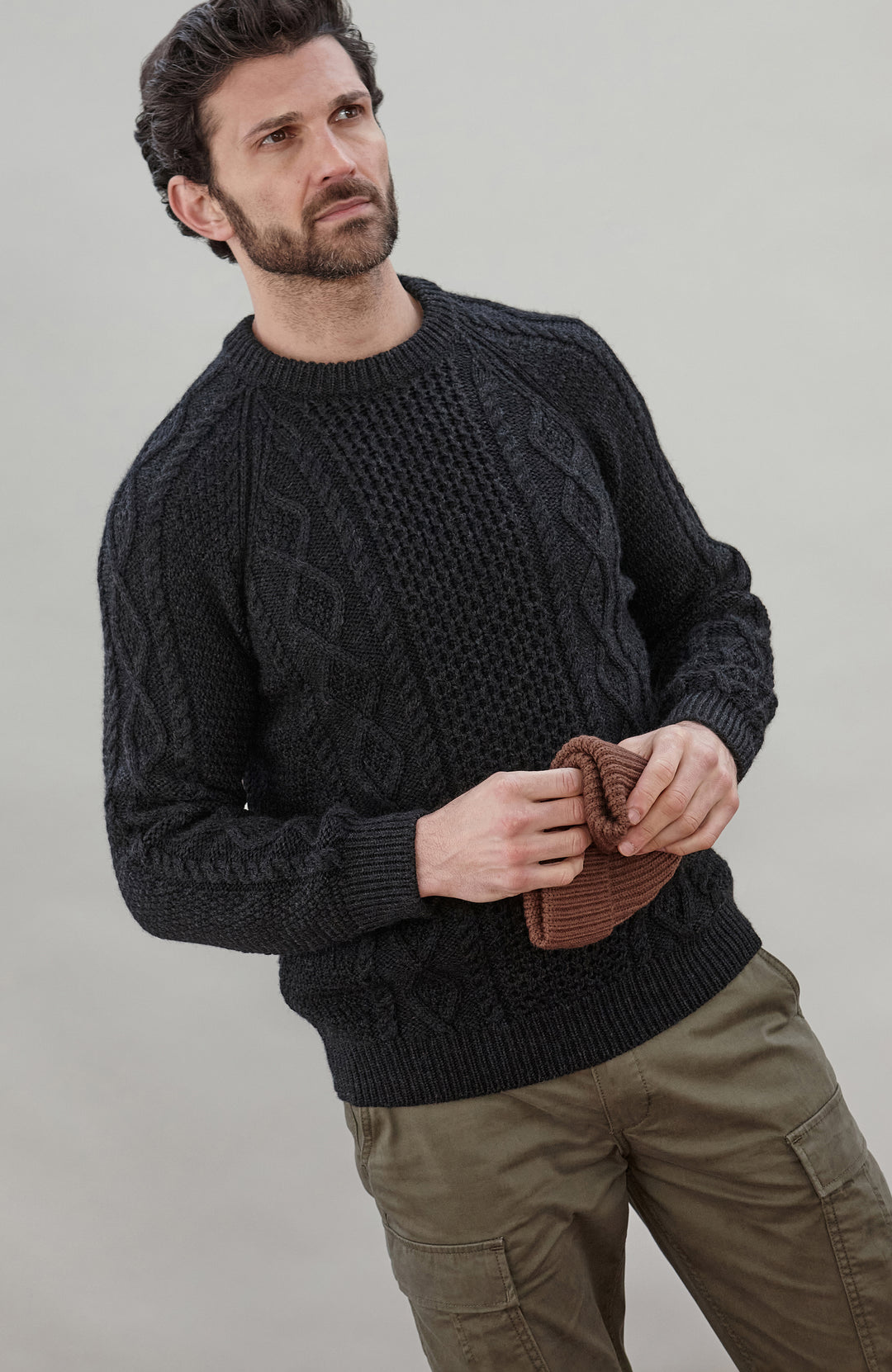 Man wearing a black wool cable sweater Made in Engladn by Paul James Knitwear 