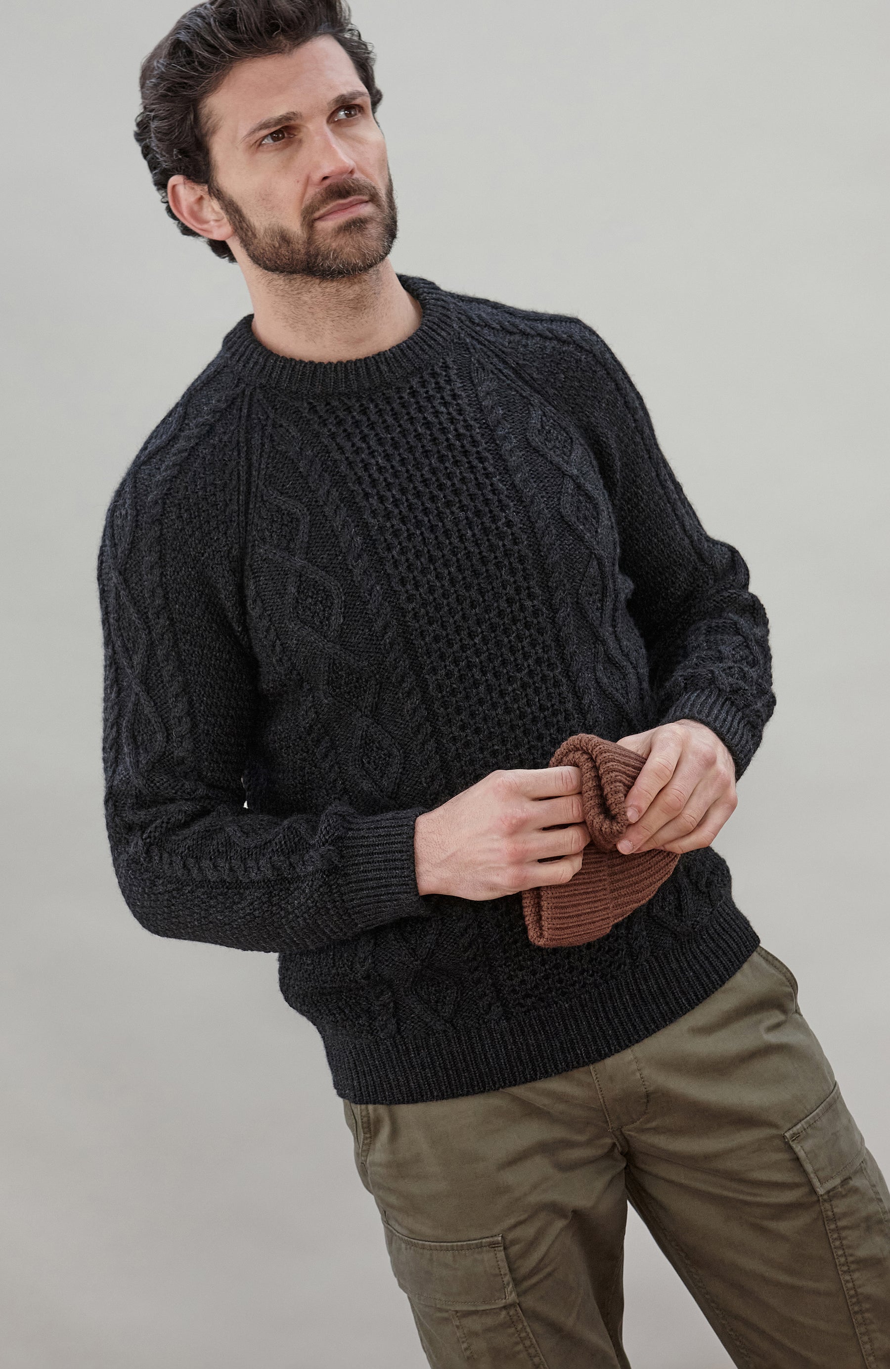 Man wearing a black wool cable sweater Made in Engladn by Paul James Knitwear 