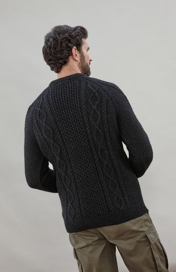 Man wearing a black wool cable sweater Made in England by Paul James Knitwear