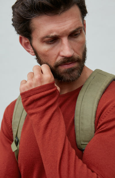 Man wearing a red merino wool sweater and green backpack against a light gray background