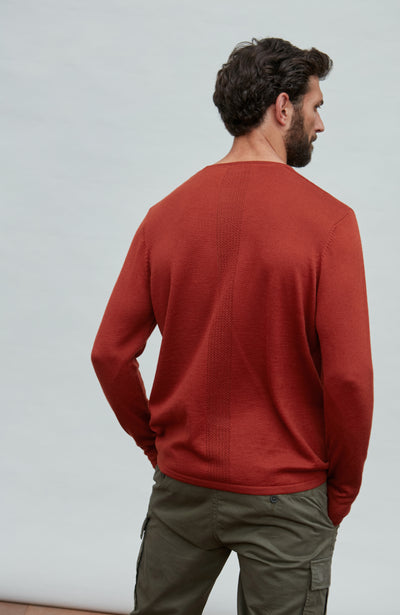 Man wearing a red wool sports sweater and green pants against a light gray background