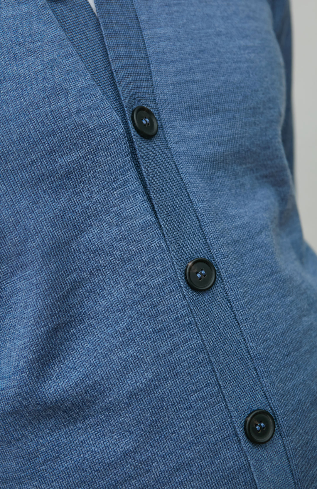 Close-up of a blue merino wool cardigan with black buttons on a plain background by Paul James