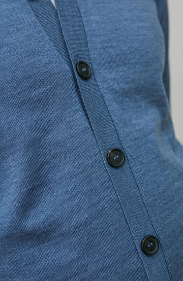 Close-up of a blue merino wool cardigan with black buttons on a plain background by Paul James