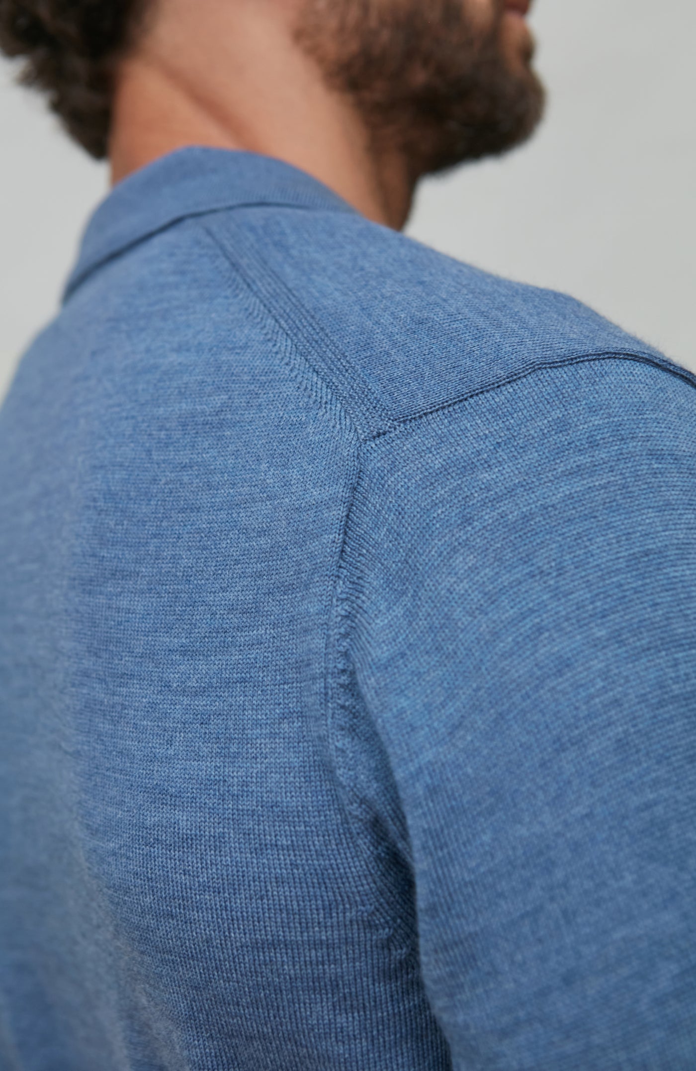 Close-up of a person wearing a blue merino wool shirt against a gray background