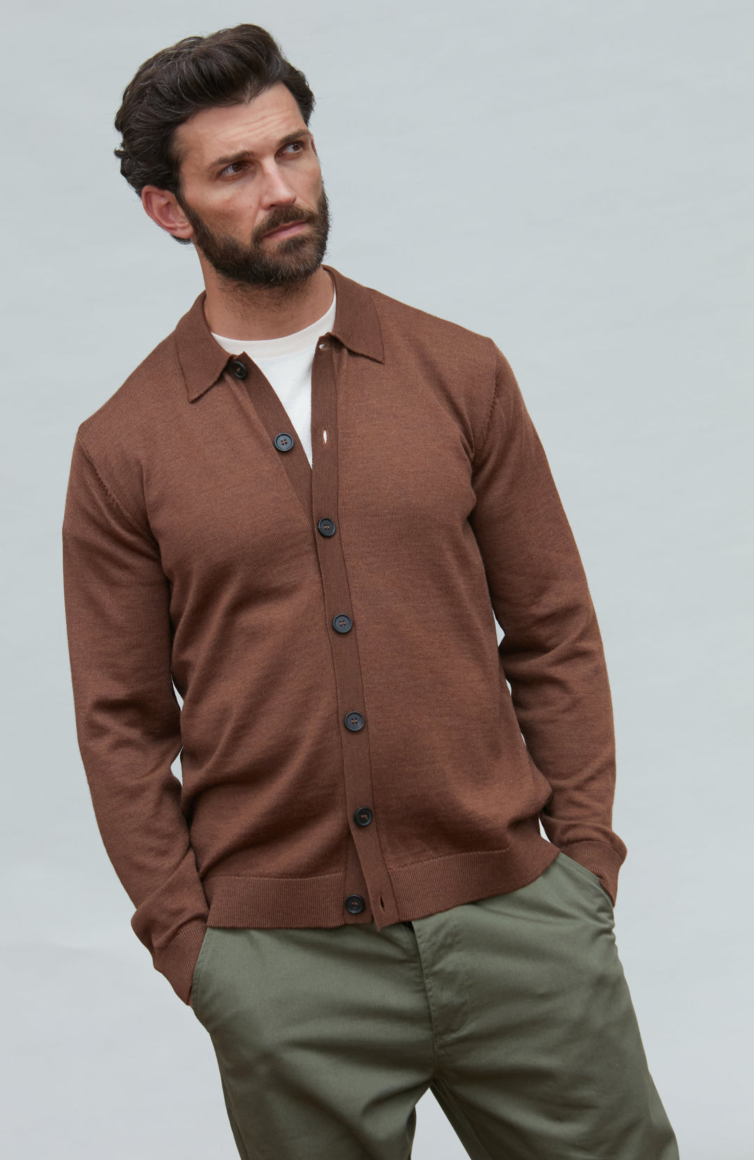 Man wearing a fine ool brown button-up shirt and green pants against a light gray background by Paul James