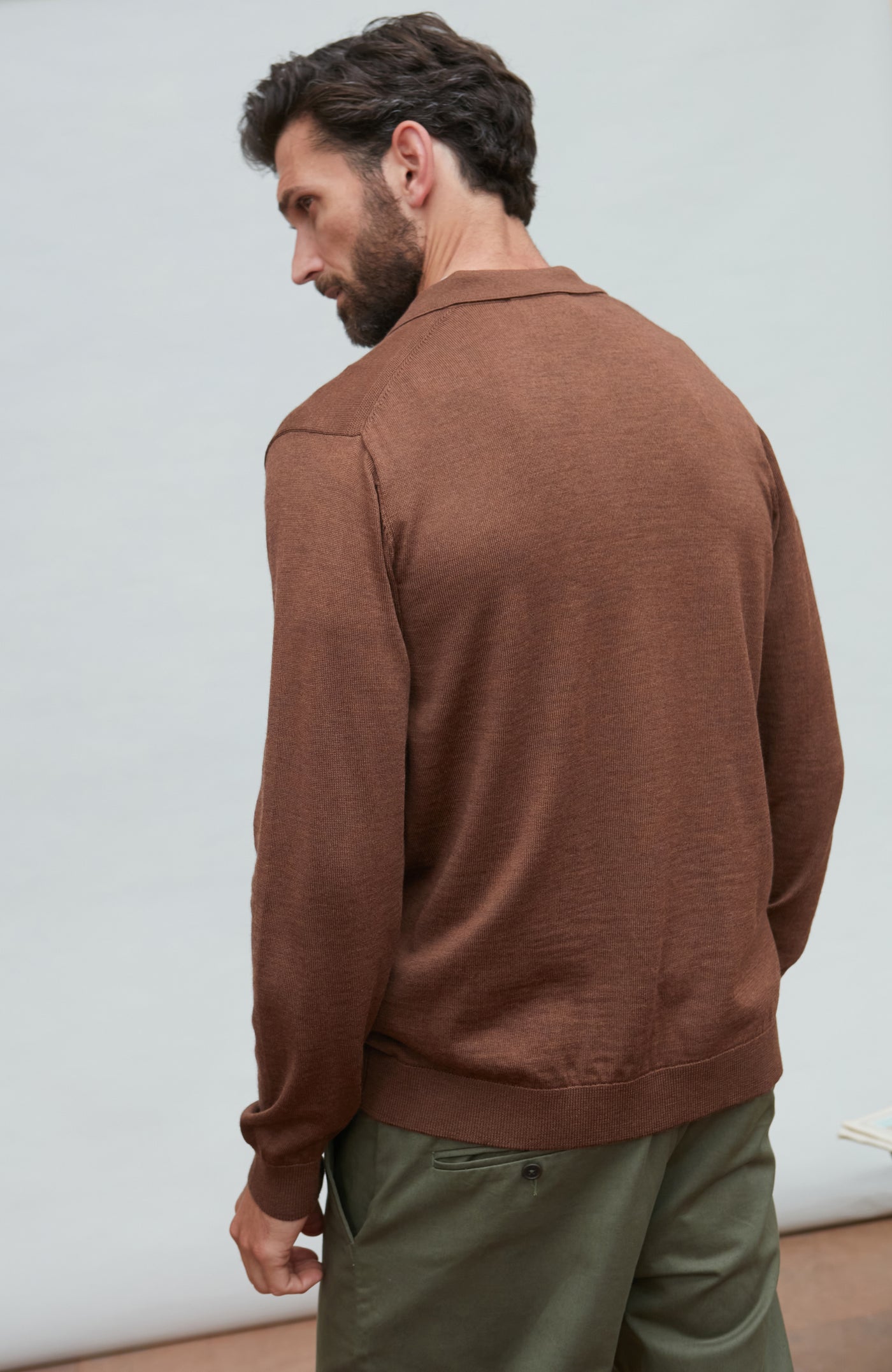 Man wearing a brown fine wool cardigan and green pants against a light gray background