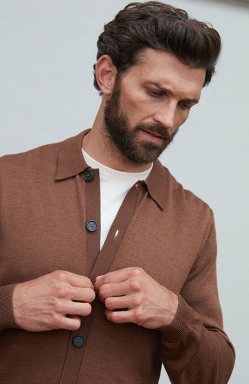 Man wearing a brown fine wool cardigan with a white shirt underneath, against a plain background by Paul James
