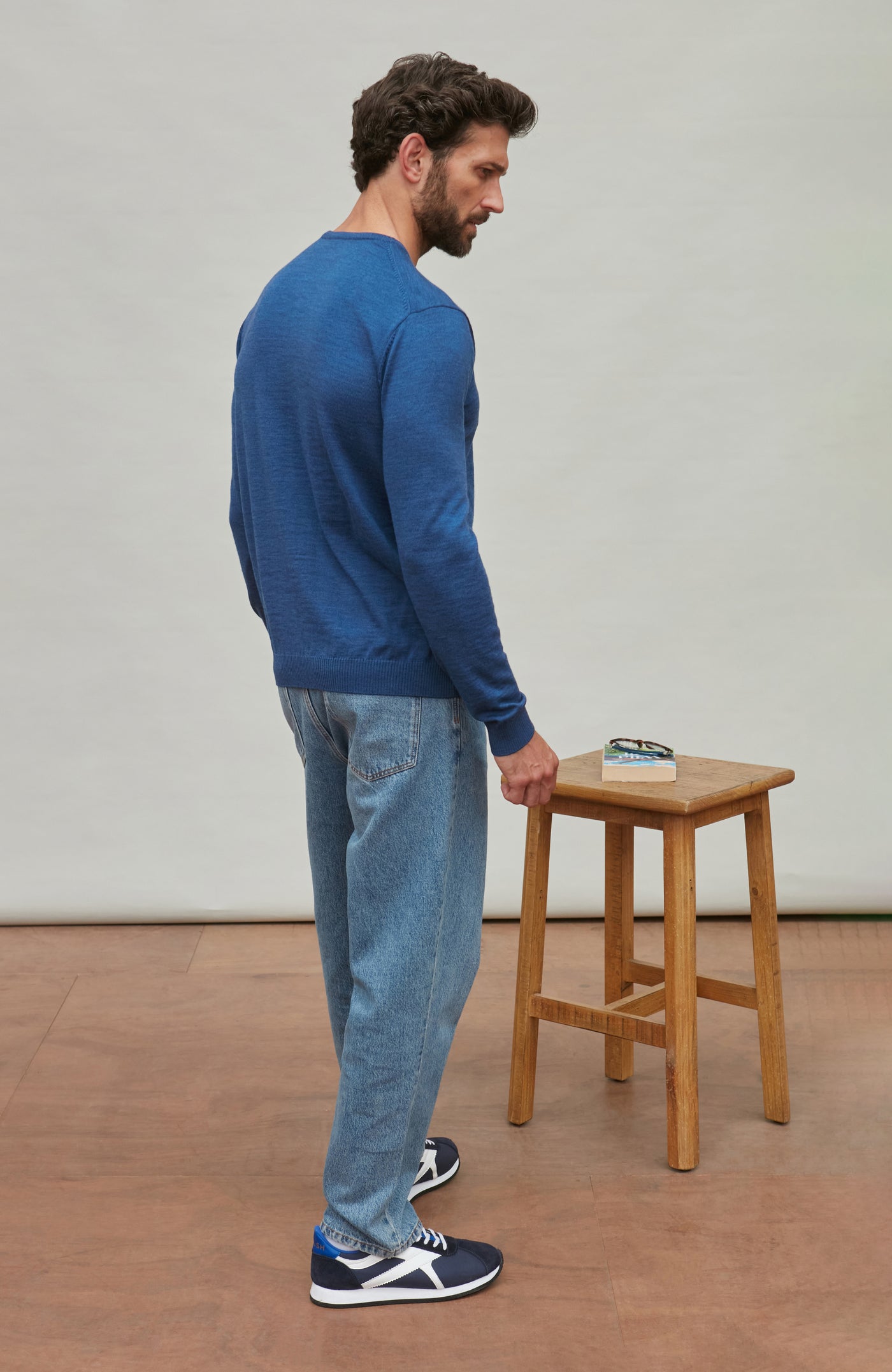 Man wearing a blue fine merino wool sweater against a gray background