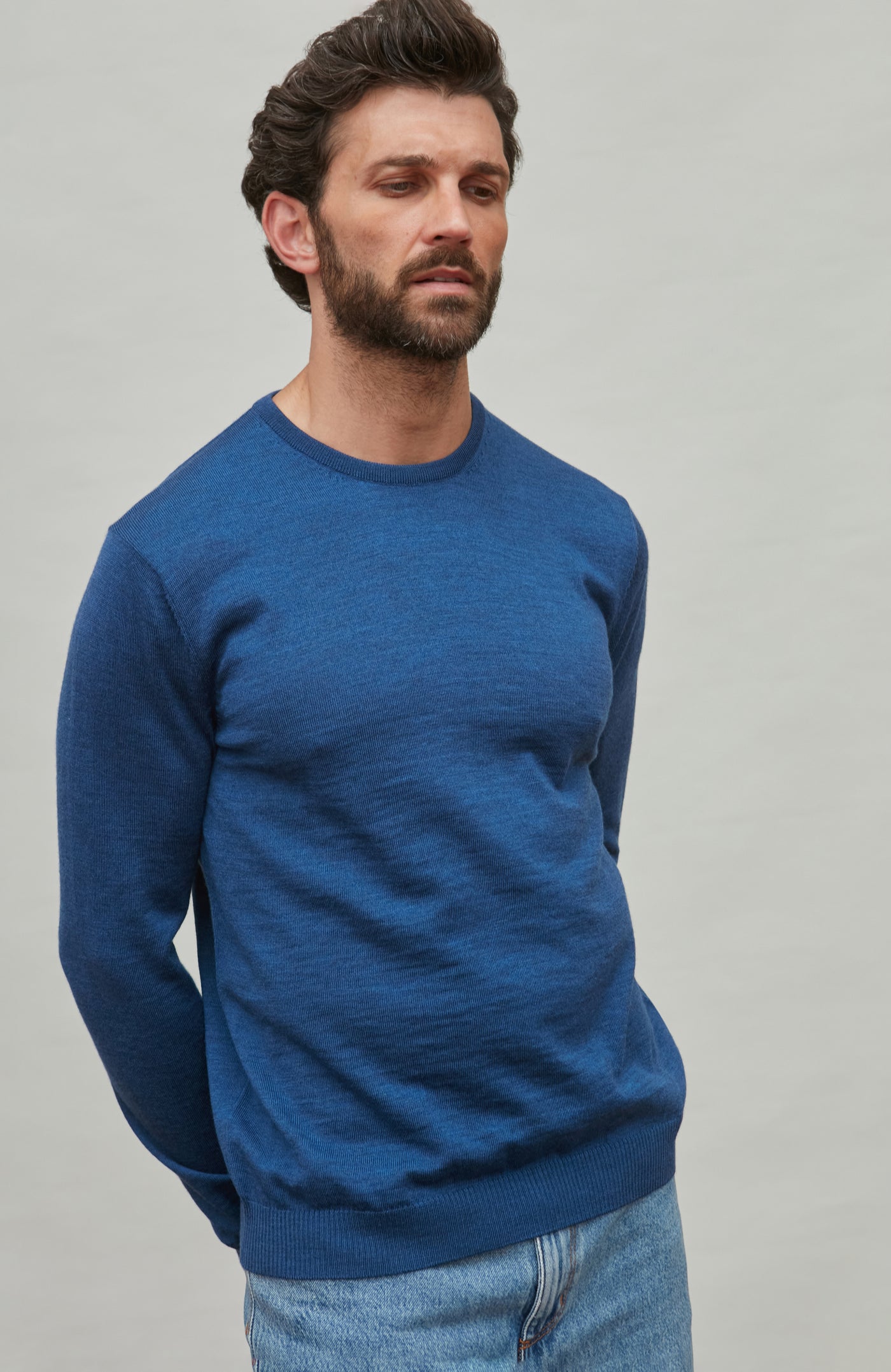 Man wearing a blue fine merino wool sweater against a gray background