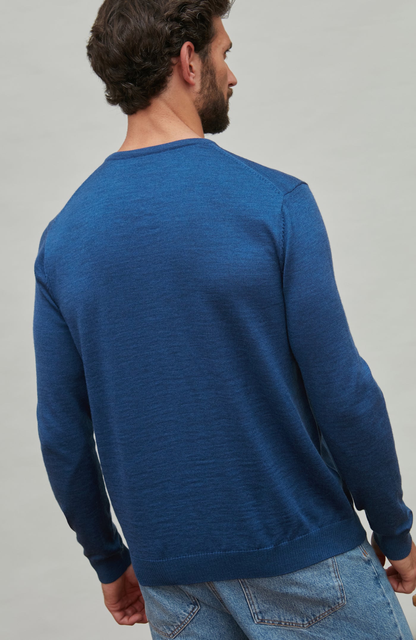 Man wearing a blue fine merino wool sweater against a gray background
