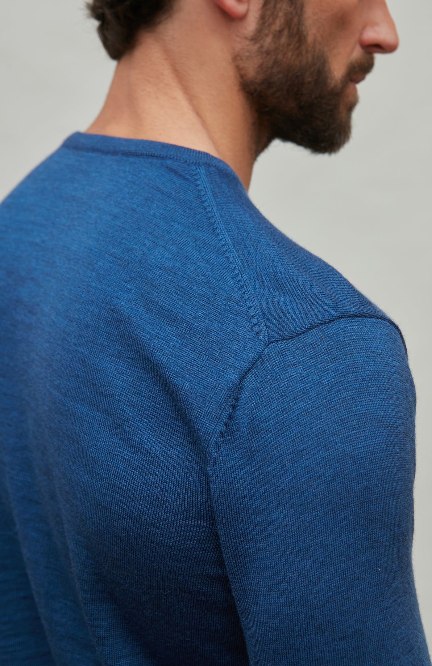 Man wearing a blue fine merino wool sweater against a gray background