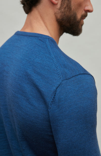 Man wearing a blue fine merino wool sweater against a gray background