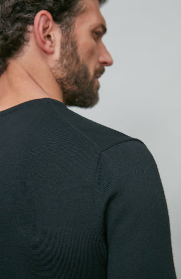 Man wearing a black v neck sweater against a light gray background
