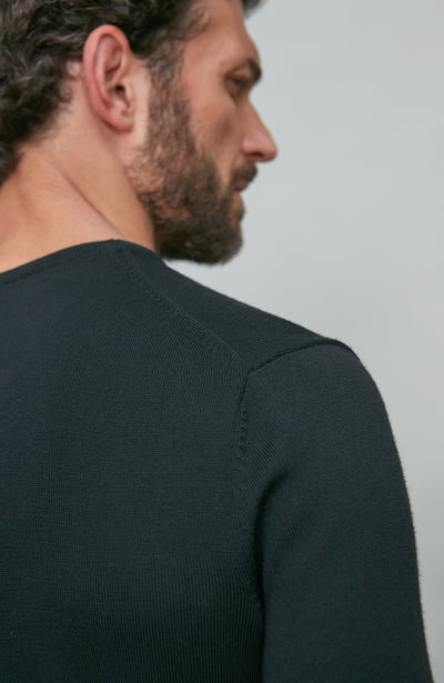 Man wearing a black v neck sweater against a light gray background