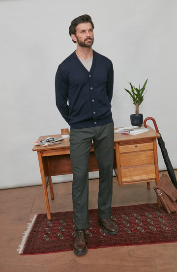 Man wearing a navy merino wool cardigan over a white shirt, standing in a room with a wooden desk and rug.