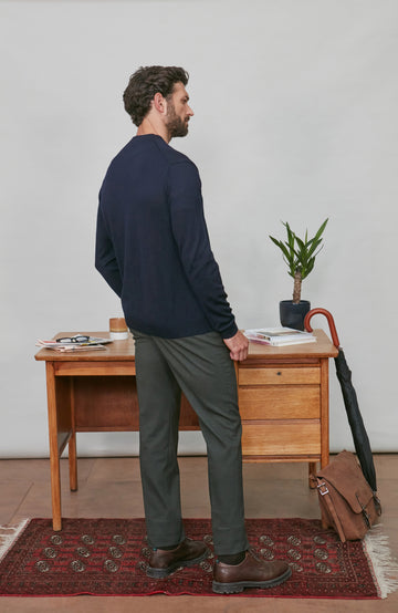 Man wearing a merino wool cardigan standing in a room with a wooden desk and plant