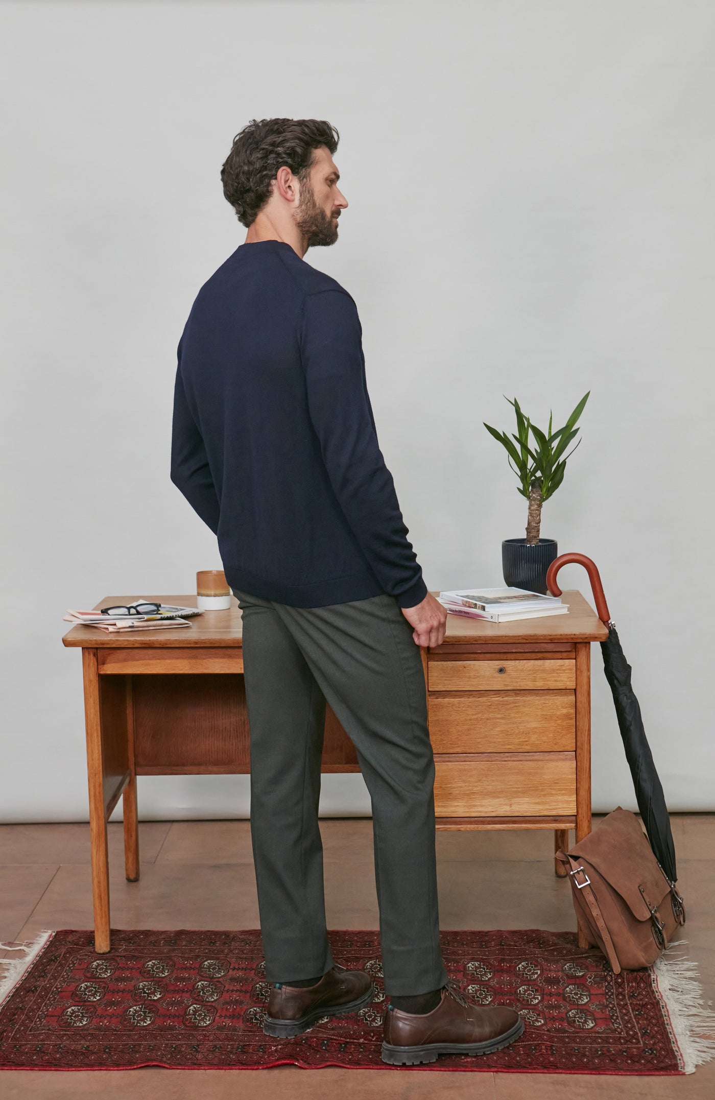 Man wearing a merino wool cardigan standing in a room with a wooden desk and plant