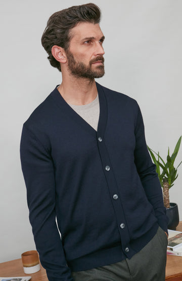 Man wearing a navy merino wool cardigan standing indoors with a neutral background