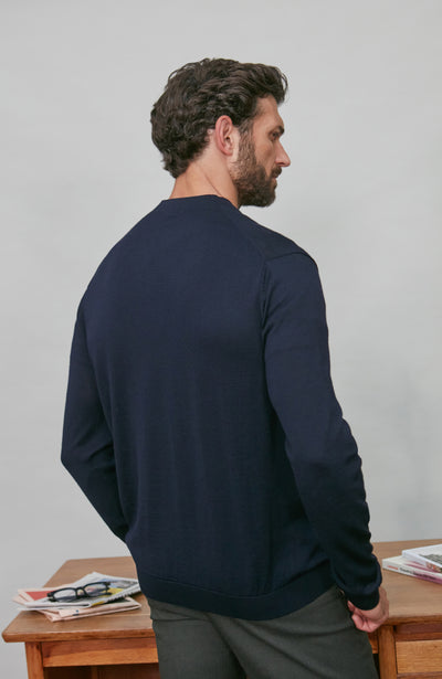 Man wearing a navy blue merino wool cardigan standing in front of a wooden desk with newspapers on it.