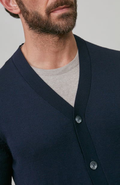 Man wearing a navy merino wool cardigan over a gray shirt against a plain background