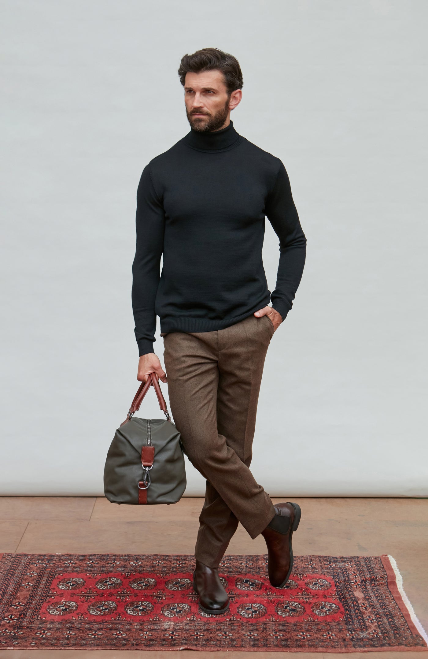 Man wearing a black fine merino wool turtleneck sweater against a gray background