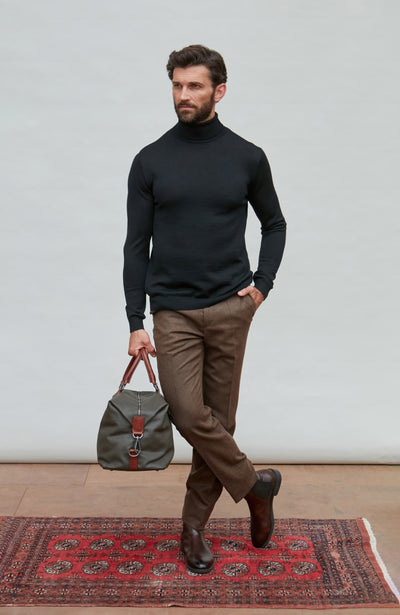 Man wearing a black fine merino wool turtleneck sweater against a gray background