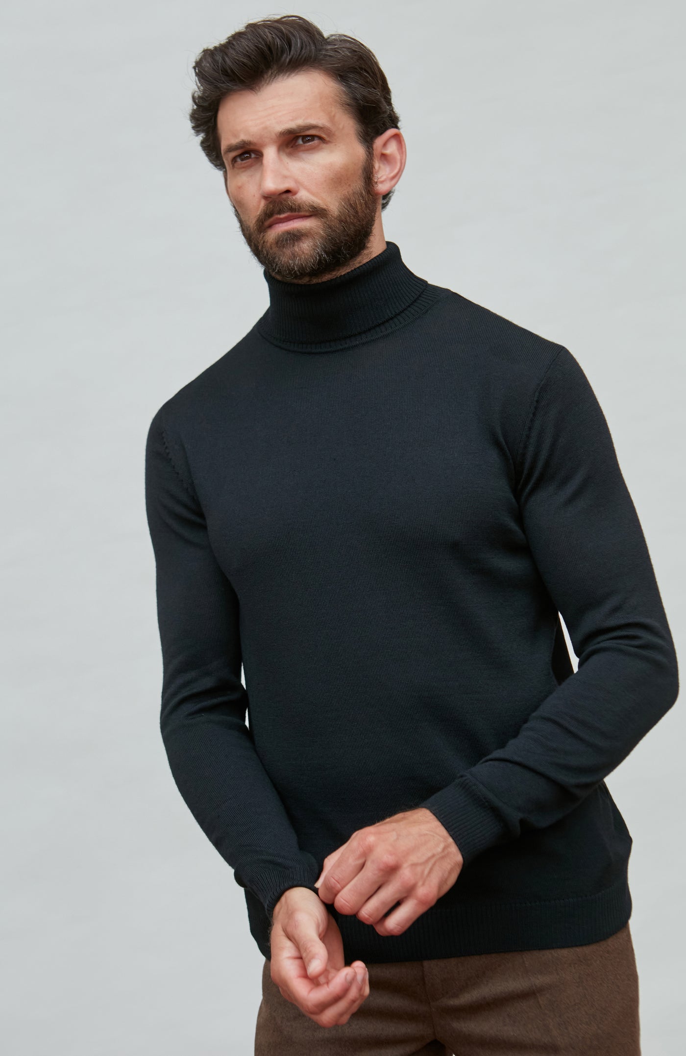 Man wearing a black fine merino wool turtleneck sweater against a gray background