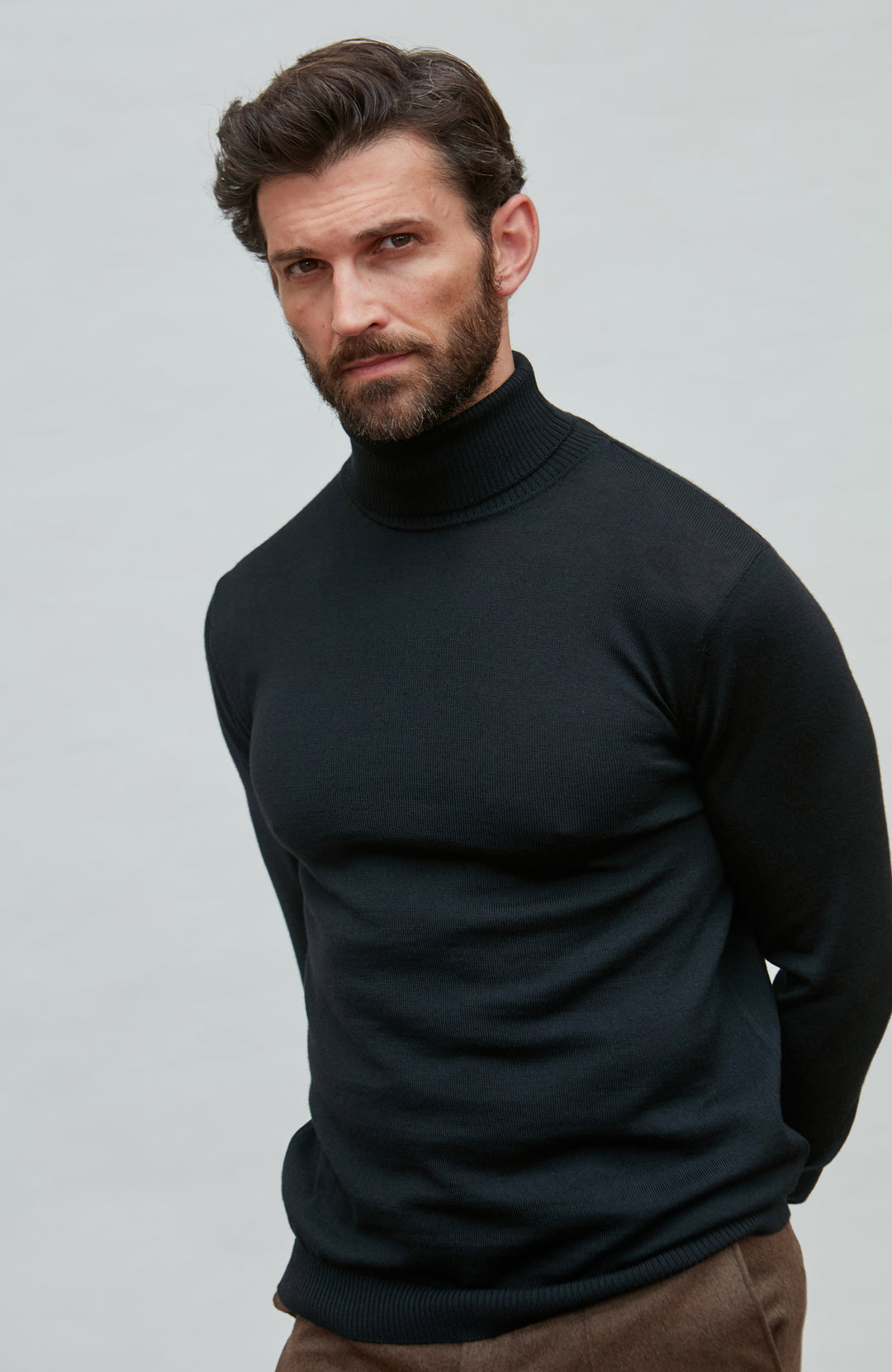 Man wearing a black fine merino wool turtleneck sweater against a gray background by Paul James