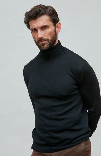 Man wearing a black fine merino wool turtleneck sweater against a gray background