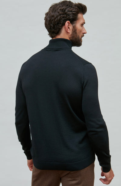 Man wearing a black fine merino wool turtleneck sweater against a gray background