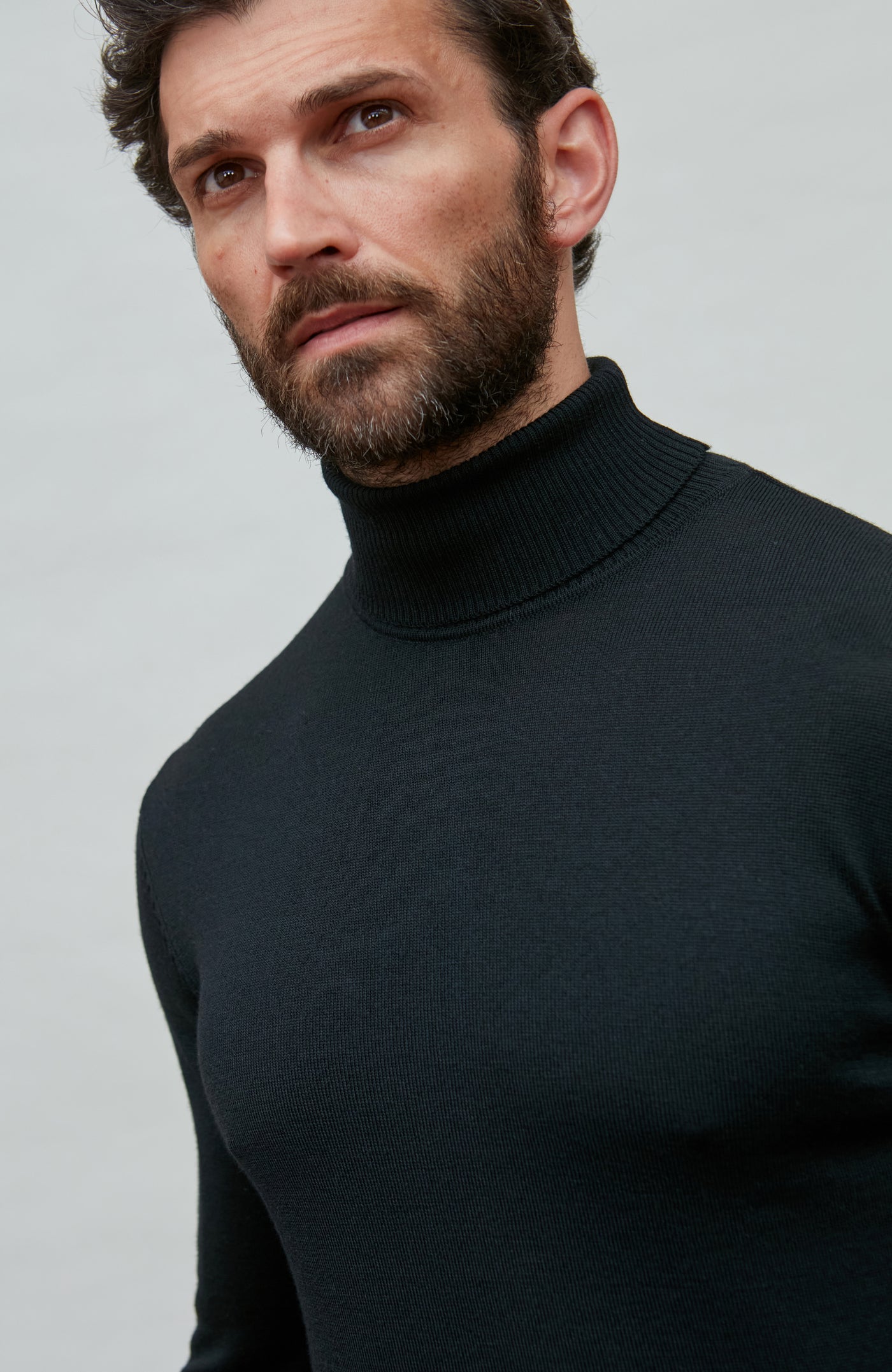 Man wearing a black fine merino wool turtleneck sweater against a gray background
