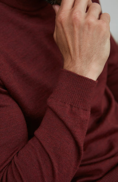 Man wearing a red merino wool mock turtleneck sweater sitting on a chair.