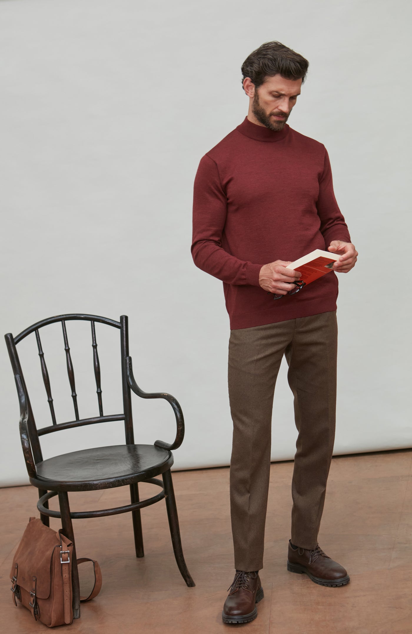 Man wearing a red merino wool mock turtleneck sweater sitting on a chair.