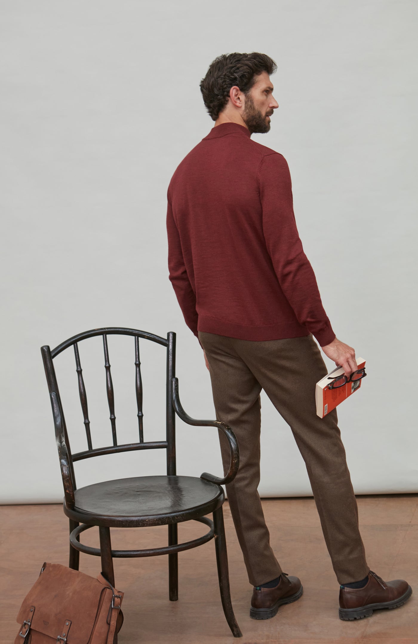 Man wearing a red merino wool mock turtleneck sweater sitting on a chair.