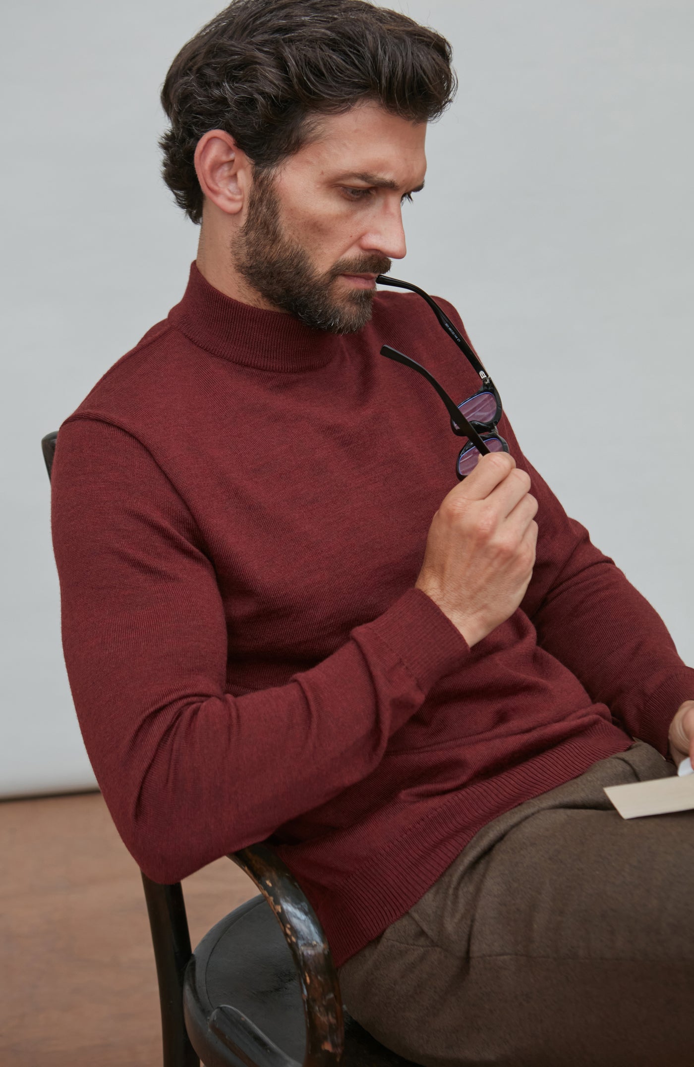 Man wearing a red merino wool mock turtleneck sweater sitting on a chair.