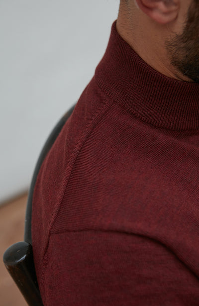 Man wearing a red merino wool mock turtleneck sweater sitting on a chair.