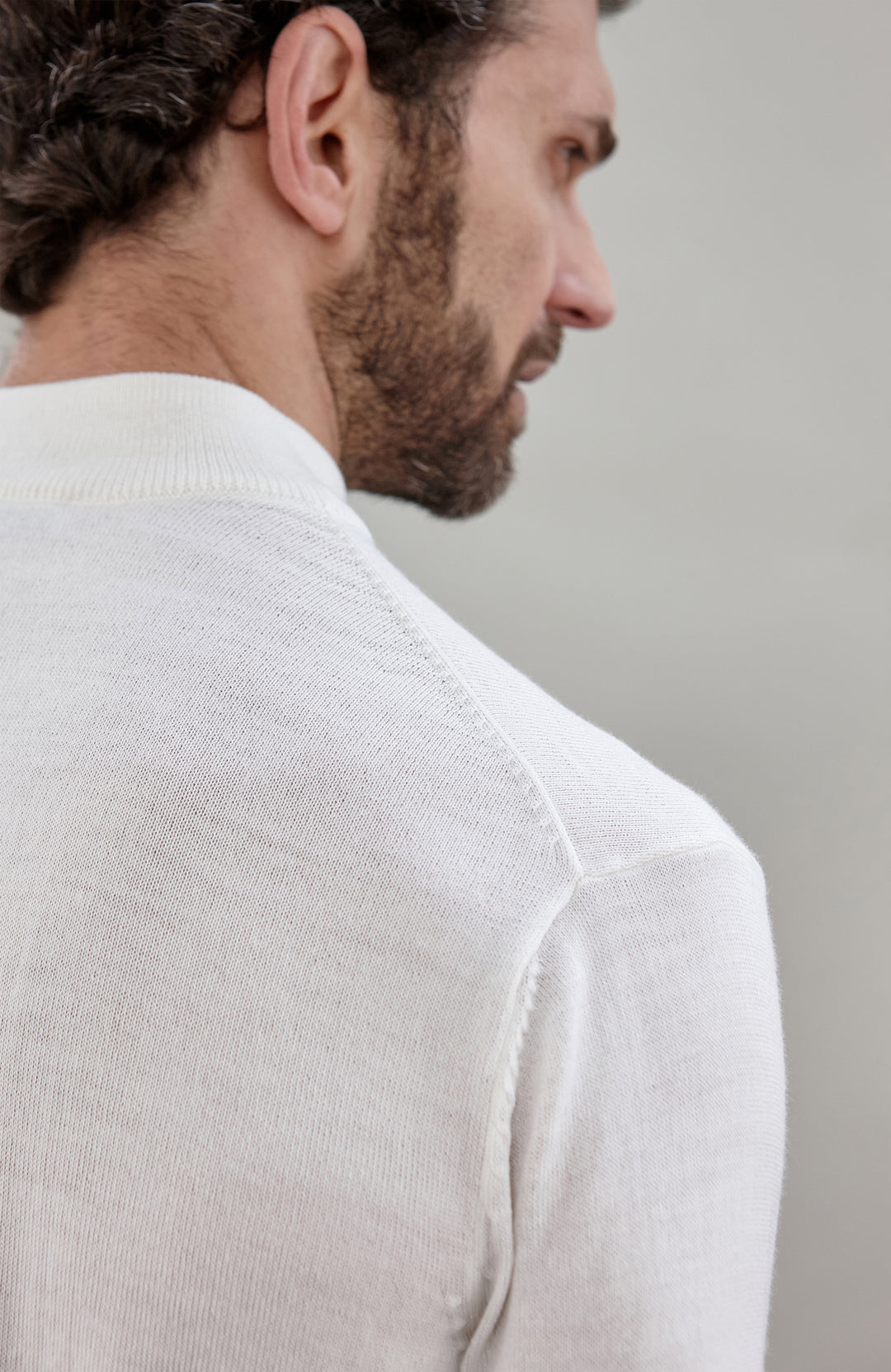 Close-up side profile of a man wearing a light cream fine merino wool knit sweater, showing the texture of the fabric and the back of the neck.