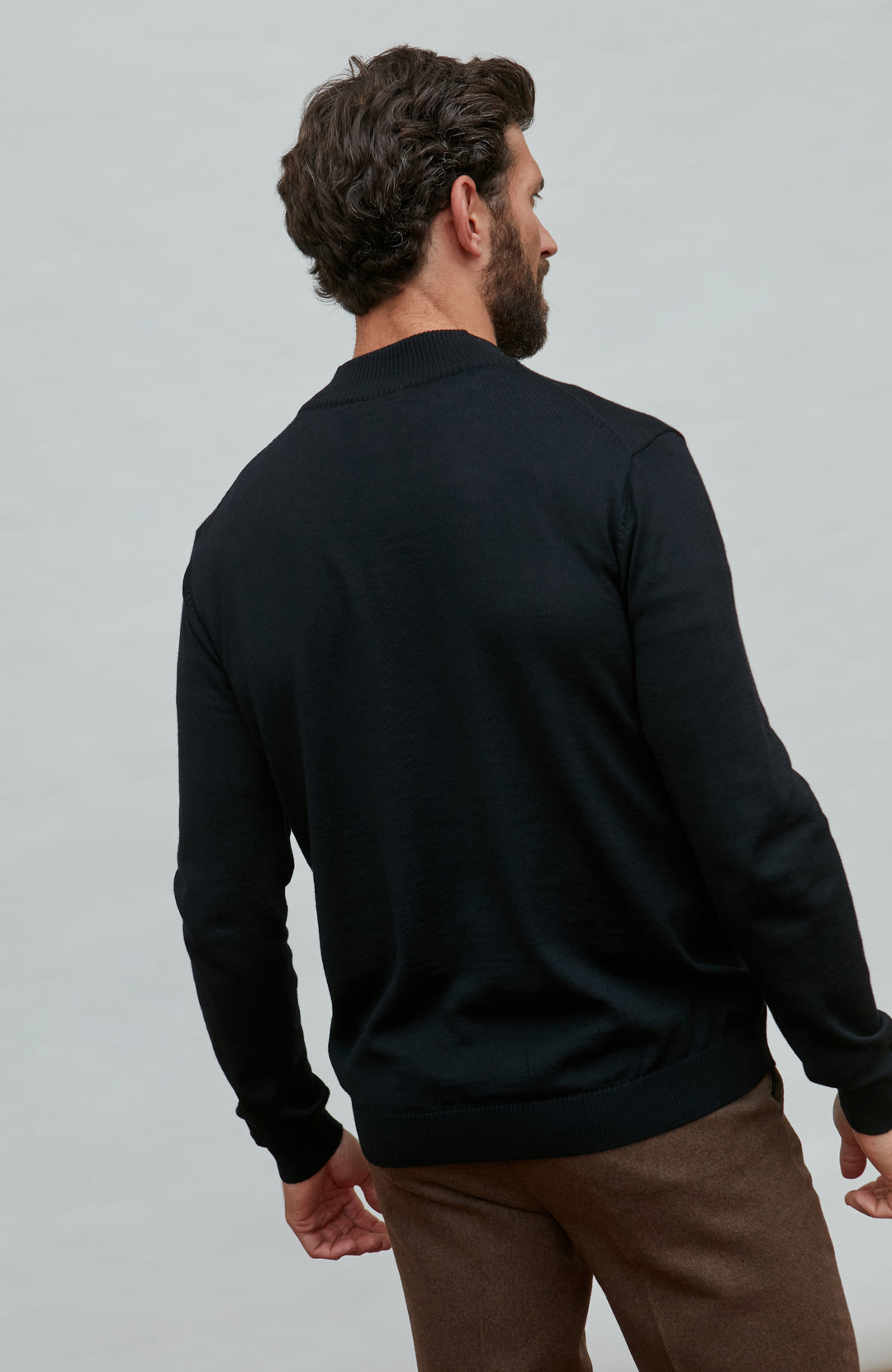 Man wearing a black quarter-zip merino wool sweater against a gray background