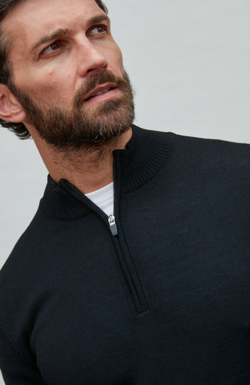 Man wearing a black quarter-zip merino wool sweater against a gray background