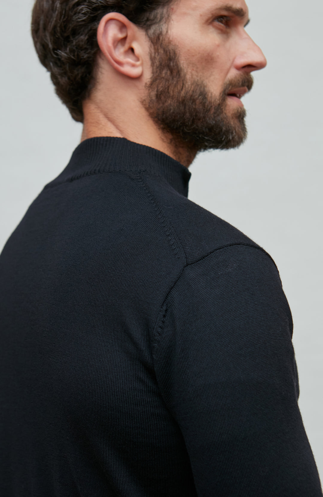 Man wearing a black quarter-zip merino wool sweater against a gray background