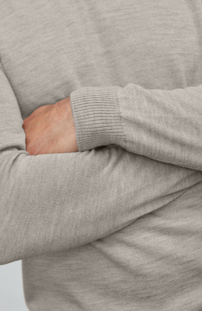 Close-up of a person wearing a gray sweater with one arm crossed over the other.