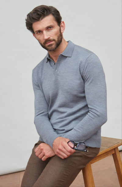Man wearing a light grey polo neck merino wool sweater sitting on a wooden bench against a plain background