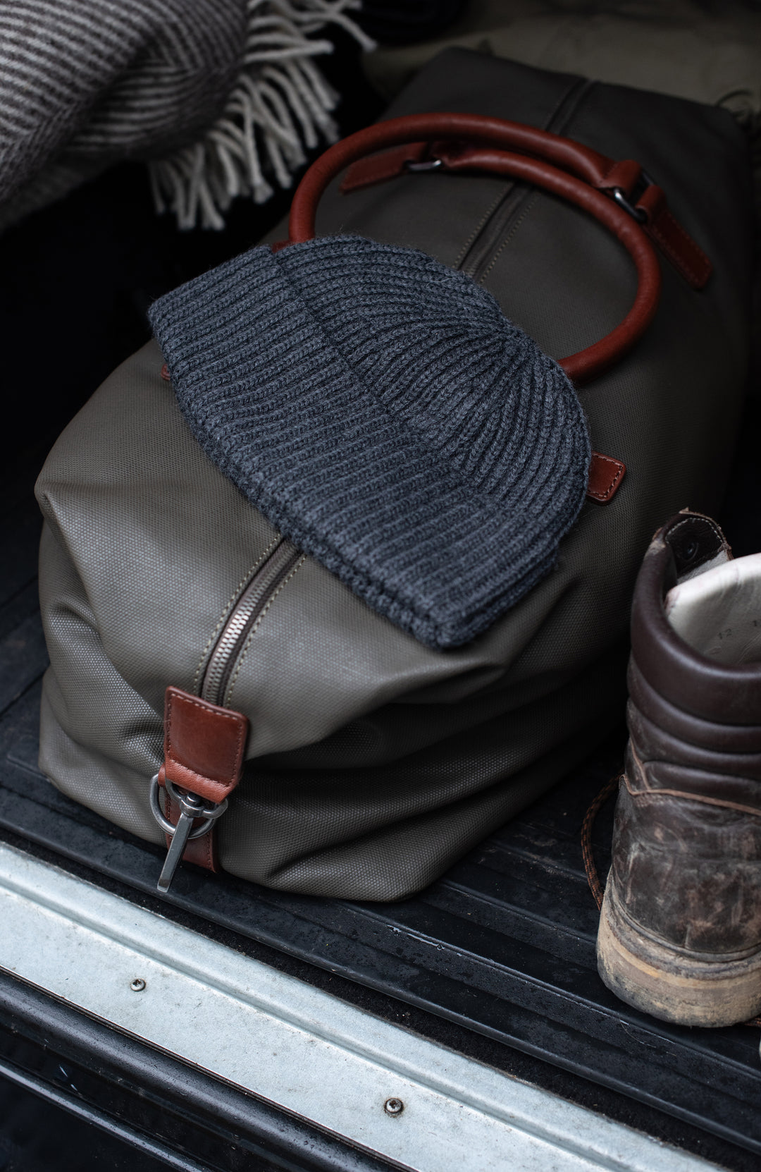 Gray bag with a grey fisherman wool knit cap and brown boot on a vehicle's open door.