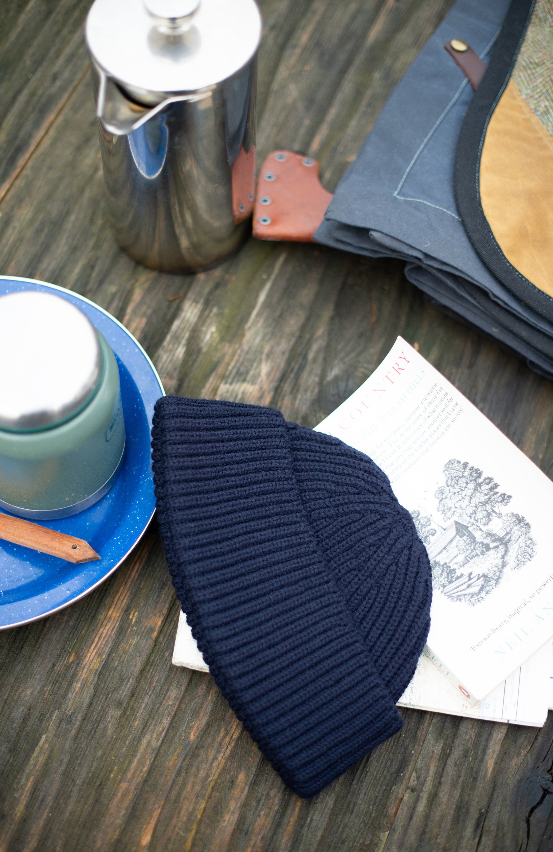 Navy wool fisherman knit beanie on a wooden surface with a teapot and saucer in the background