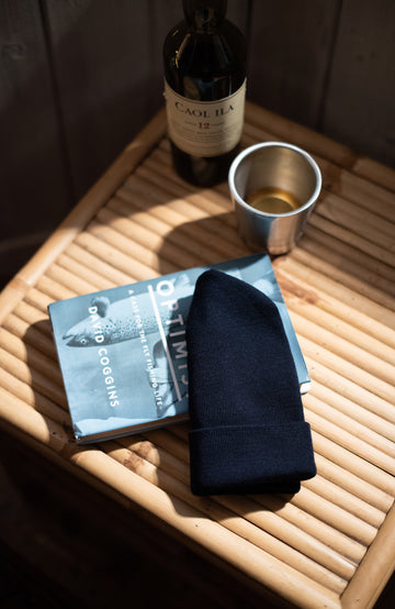 navy wool beanie Bottle of Caol Ila whiskey, silver tumbler, and black napkin on a wooden tray.